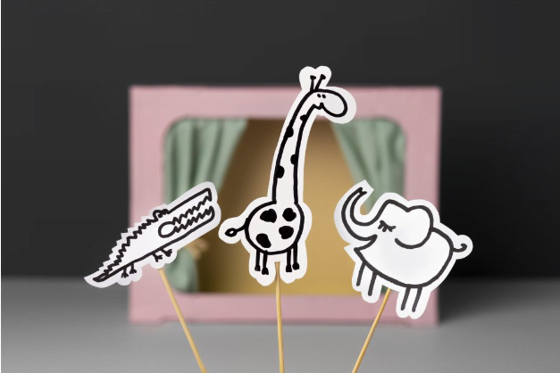 Um jacaré, uma girafa e um elefante feitos de desenhos em papel e recortados estão com palitos de madeira colados juntos fazendo fantoches.